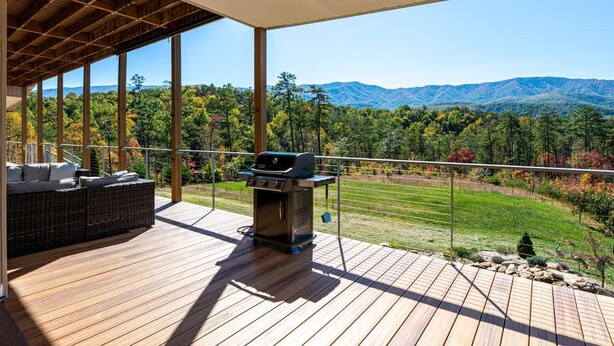 Terraza de madera con una parrilla y zona de estar, con vistas a un paisaje montañoso.