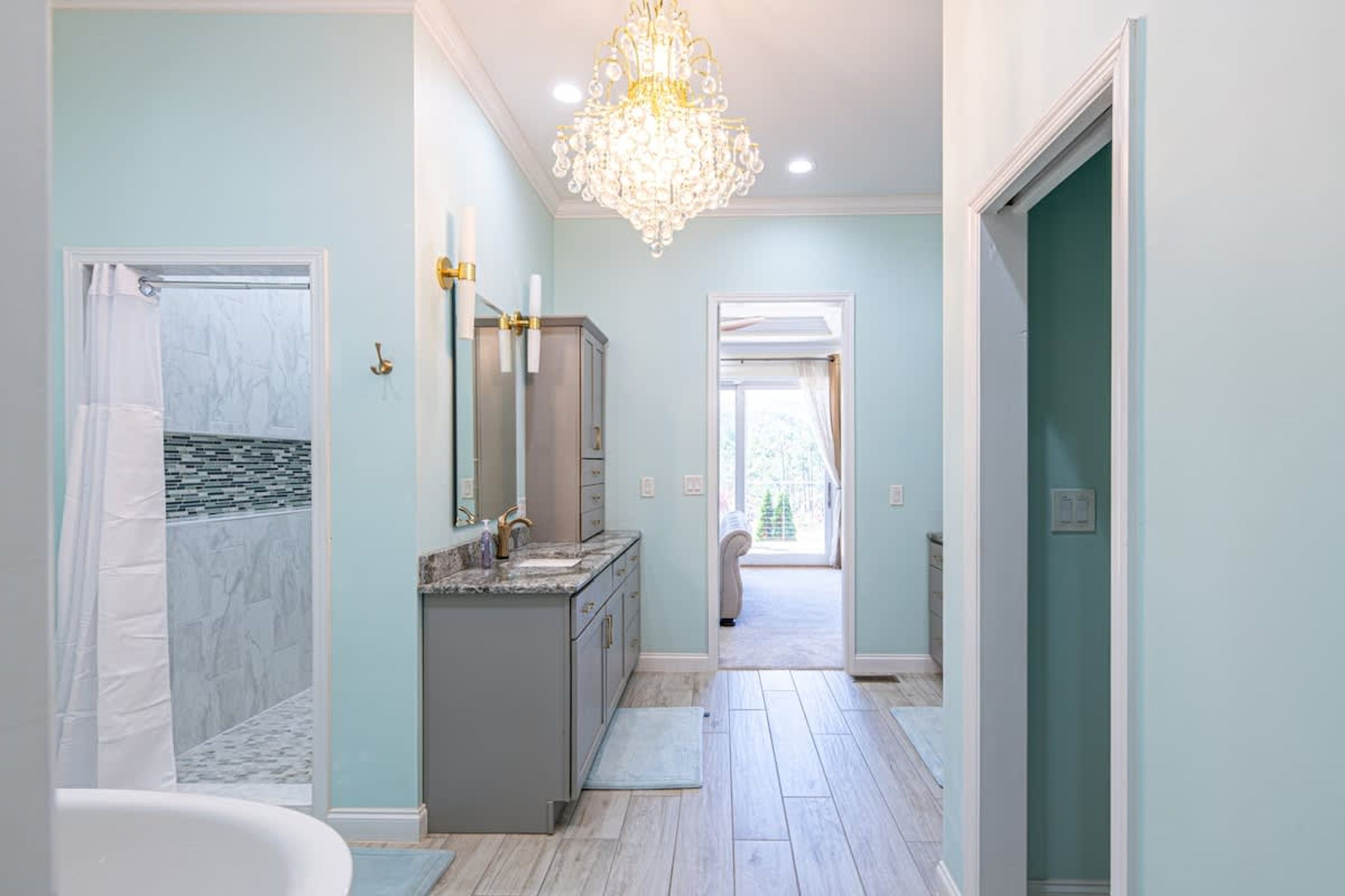 A modern bathroom with a marble shower, a large vanity, and a chandelier.