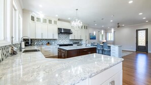 Una cocina amplia con una isla grande de mármol, armarios blancos y una lámpara moderna.