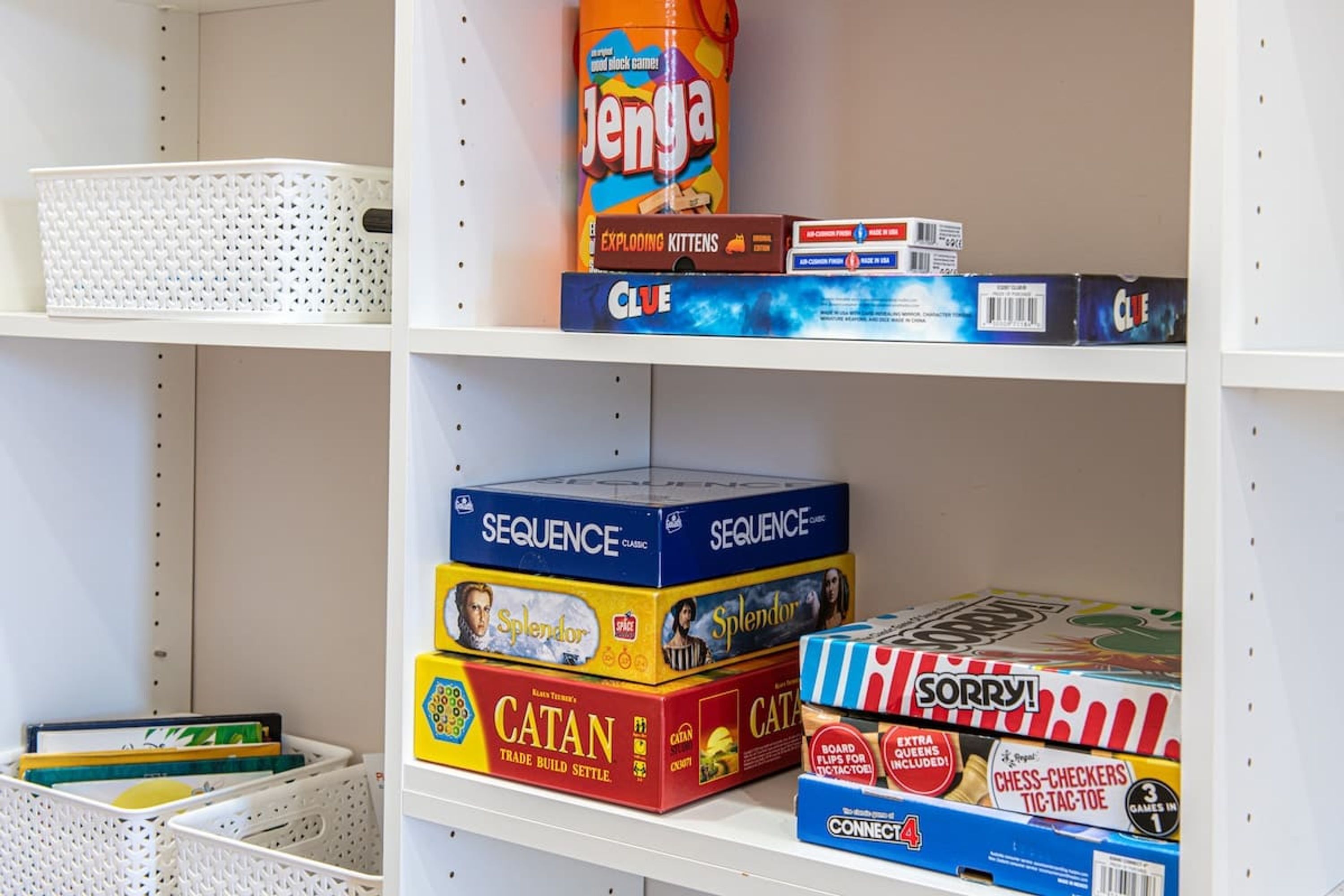 Ein Regal mit verschiedenen Gesellschaftsspielen, darunter 'Jenga', 'Clue', 'Sequence', 'Splendor', 'Catan' und 'Sorry!'.