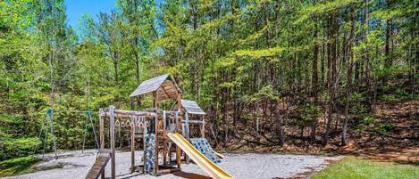 A wooden playground with slides and swings set in a forested area.