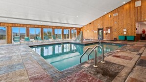 Una amplia piscina interior con pared de madera y grandes ventanales.