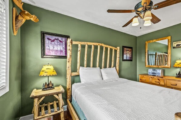 A bedroom with a wooden headboard, a bed with white bedding, a small bedside table with a lamp, a ceiling fan, and a dresser with a mirror. - Sleeps 4 Hot Tub Indoor Pool Mountain Views (Gatlinburg)