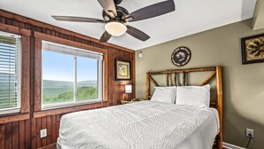 Ein Schlafzimmer mit einem großen Bett, Holzwänden, einem Deckenventilator, einem Fenster mit Blick und einer Uhr an der Wand.