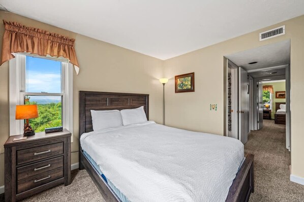 A bedroom with a large bed, a nightstand with a lamp, a window with a view, and a door leading to another room. - Sleeps 6 Indoor Pool Hot Tub Mountain Views (Gatlinburg)