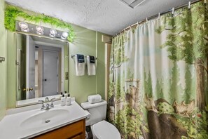 A bathroom with a white sink, mirror, and toilet. There is a shower curtain with a forest and moose design. - Sleeps 6 Indoor Pool Hot Tub Mountain Views (Gatlinburg)