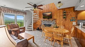 A cozy living room with a fireplace, wooden walls, a dining area, and a balcony with a scenic view. - Sleeps 8 Pool Playground Mountain Views Hot Tub (Gatlinburg)