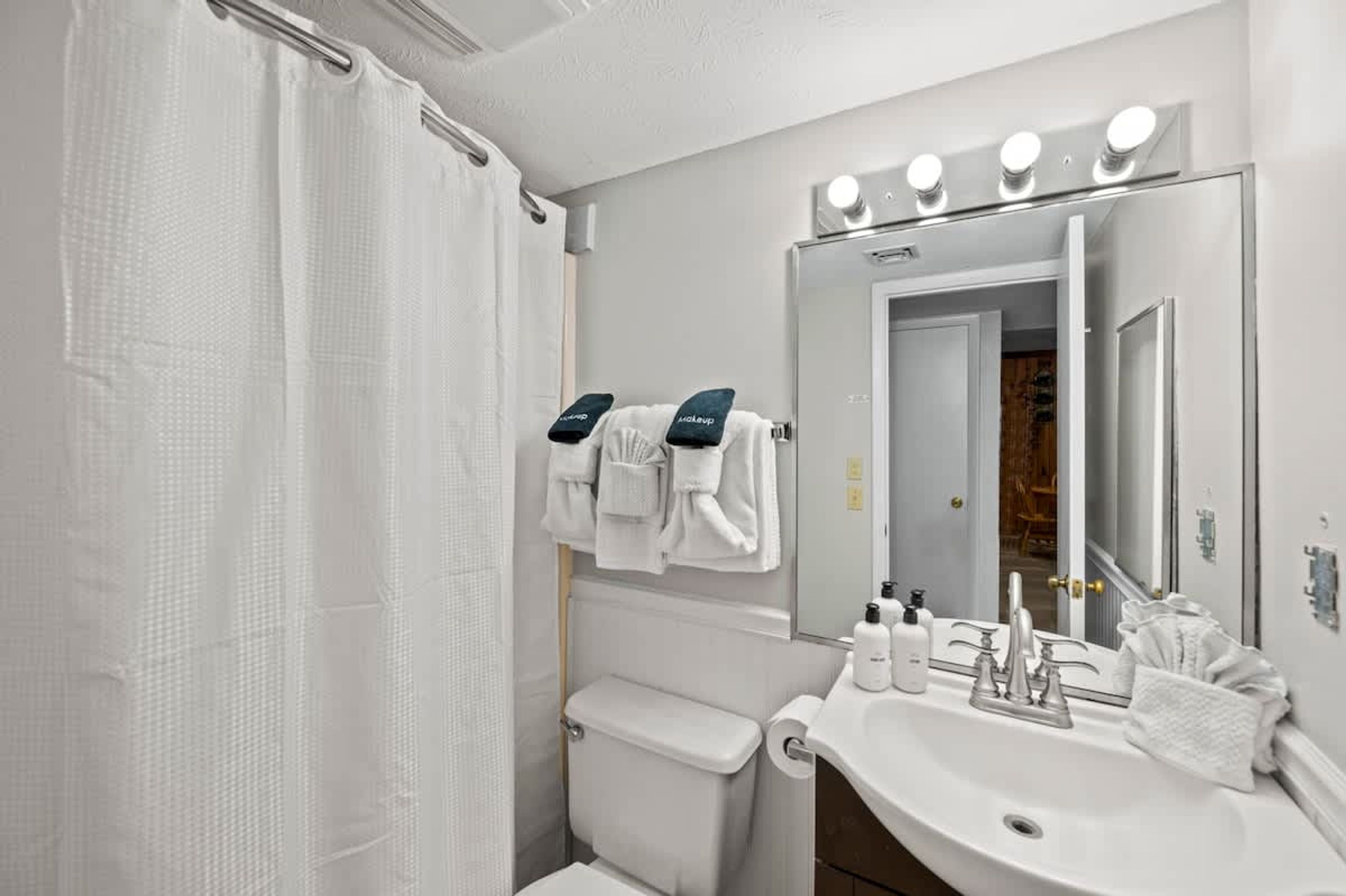 Un bagno con il water, un lavandino e uno specchio. Asciugamani appesi al muro e una tenda per la doccia.