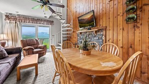 A cozy living room with a wooden dining table, comfortable seating, a fireplace, and a scenic view through the windows. - Sleeps 8 Pool Playground Mountain Views Hot Tub (Gatlinburg)