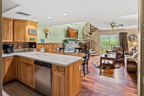 A spacious kitchen with wooden cabinets, a dishwasher, and a dining area with a table and chairs. There is a staircase leading to a balcony with a view. - Sleeps 8 Pool Playground Mountain Views Hot Tub (Gatlinburg)