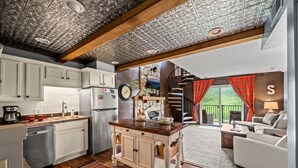 A kitchen with white cabinets, a wooden island, and a clock. There is a dining area with a sofa and a window with red curtains. - Sleeps 6 Pool Playground Mountain Views Hot Tub (Gatlinburg)