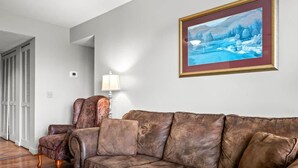 A living room with a brown leather sofa, a chair, and a painting on the wall. - Indoor Pool Hot Tub Sauna Sleeps 6 Full Kitchen (Gatlinburg)