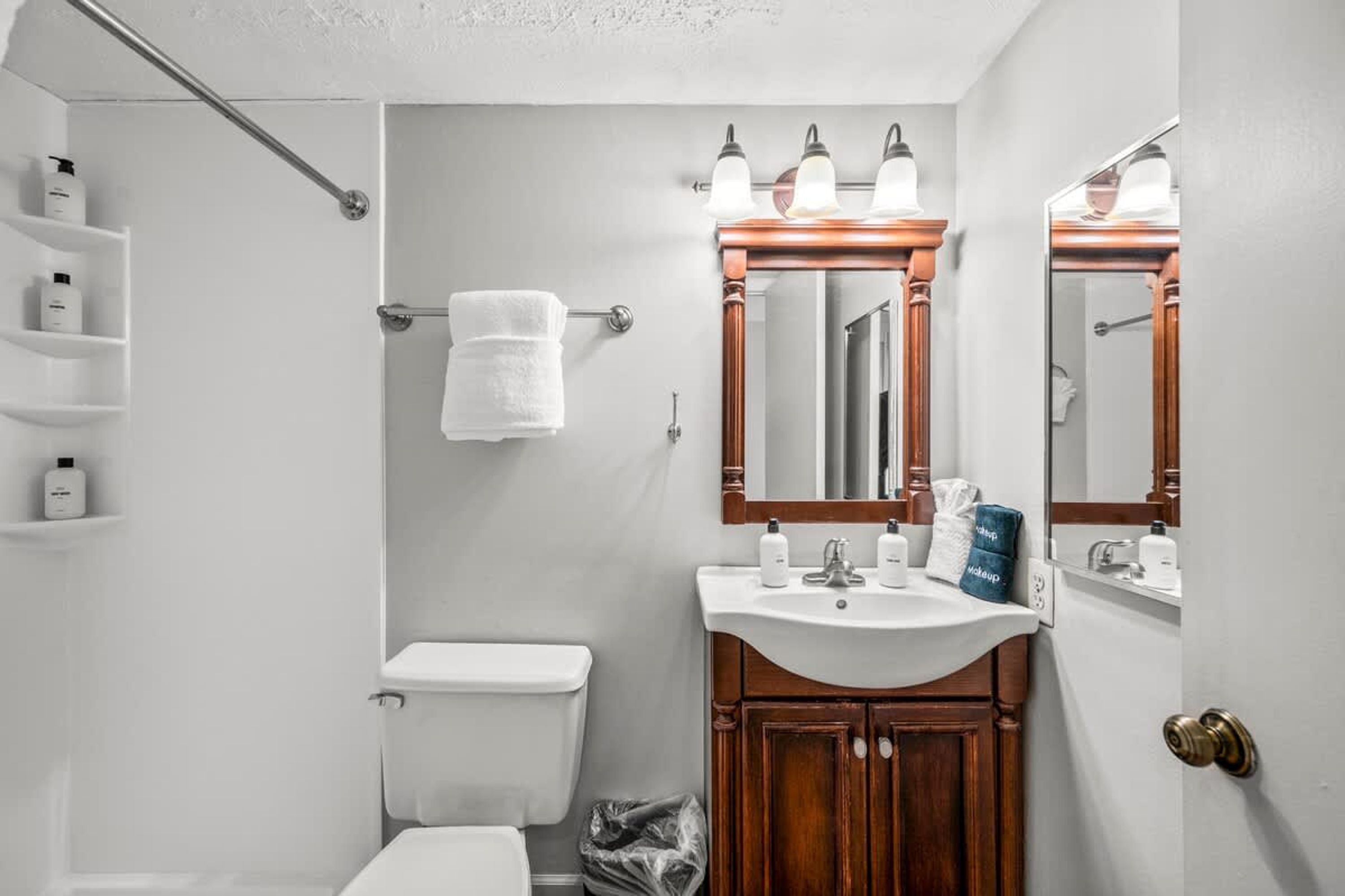 Et badeværelse med et hvidt toilet, en trækommode med spejl og en håndklædestang.