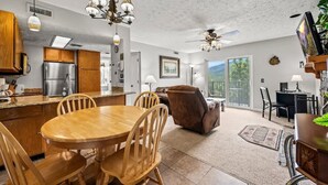 A spacious kitchen with wooden cabinets, a stainless steel refrigerator, and a dining area with a wooden table and chairs. There is a ceiling fan, pendant lights, and a large window providing natural light. - Private Balcony w Views Heated Pool Full Kitchen (Gatlinburg)