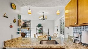 A kitchen with granite countertops, a stainless steel sink, wooden cabinets, a chandelier, and a coffee maker. - Private Balcony w Views Heated Pool Full Kitchen (Gatlinburg)