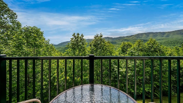 A balcony with a glass table and chairs, overlooking a forested landscape with hills in the distance. - Private Balcony w Views Heated Pool Full Kitchen (Gatlinburg)