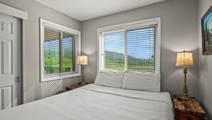 A bedroom with a bed, two bedside tables with lamps, a window with blinds, and a door. - Indoor Pool Mountain Views Hot Tub Sauna (Gatlinburg)