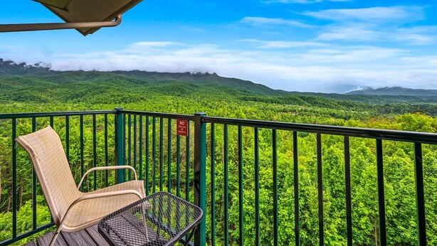 A balcony with a chair and table overlooking a lush green landscape. - Indoor Pool Mountain Views Hot Tub Sauna (Gatlinburg)