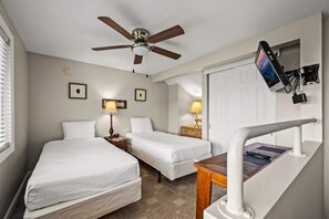 Une chambre d’hôtel avec deux lits, un ventilateur de plafond, un téléviseur fixé au mur et une petite table avec une lampe.