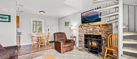 Una sala de estar con chimenea, televisor, escalera y comedor.