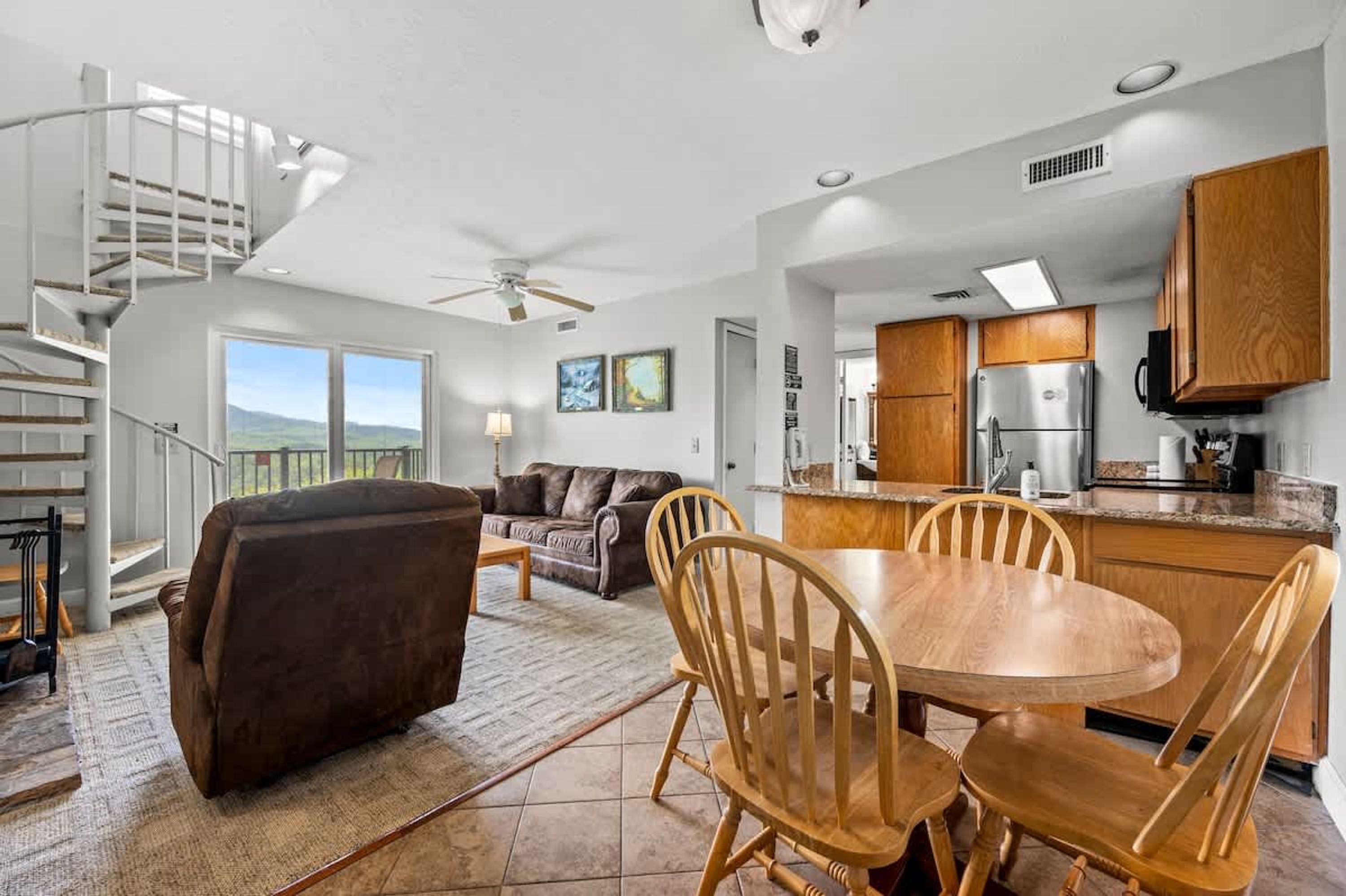 A spacious living area with a sofa, a dining table with chairs, a kitchen with wooden cabinets, and a spiral staircase.