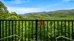 Un balcon agrémenté d’un panneau indiquant « IL EST INTERDIT DE FAIRE DES BARBECUES OU DE FUMER », donnant sur un paysage verdoyant et luxuriant avec des collines.