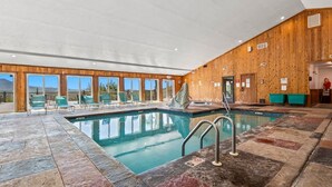 Une piscine intérieure avec un revêtement en bois, de grandes fenêtres et une vue sur l’extérieur.
