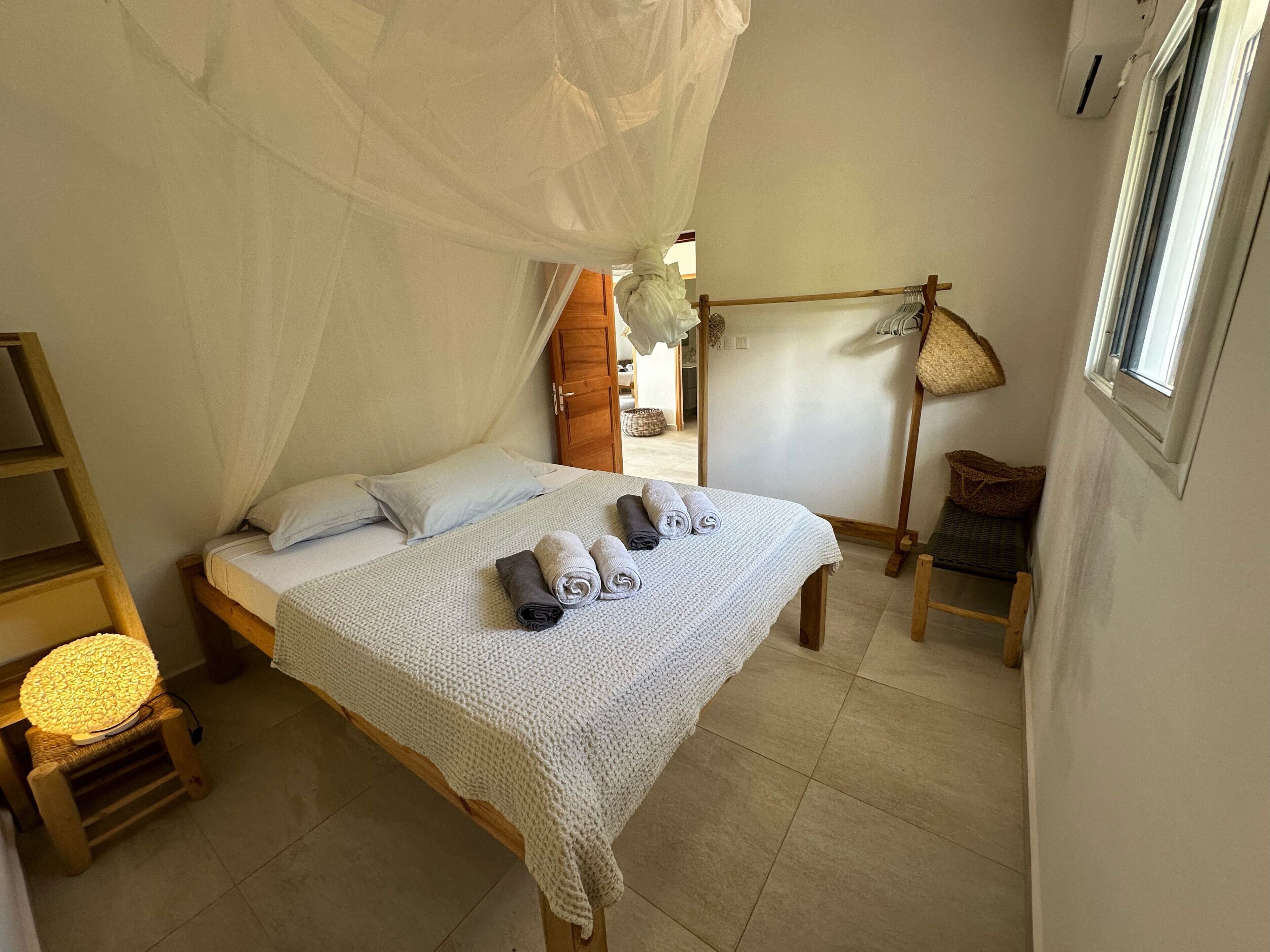 A room with a bed, a small table with a lamp, a hanging chair, and a window.