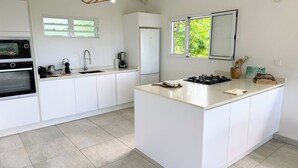 A modern kitchen with white cabinetry, a central island, a built-in oven, and a hanging light fixture. - Grey houses villa a beautiful property with a pool and spacious areas (Grand-Bourg)