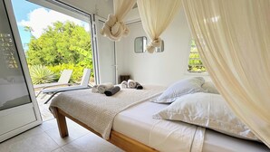 A bedroom with a bed, white curtains, and a view of the outdoors. - Grey houses villa a beautiful property with a pool and spacious areas (Grand-Bourg)