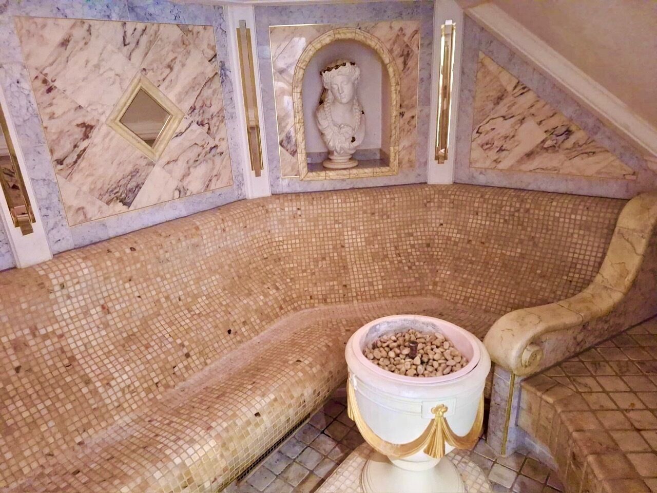 A room with a mosaic-tiled bench, a marble-patterned wall, and a decorative bust.