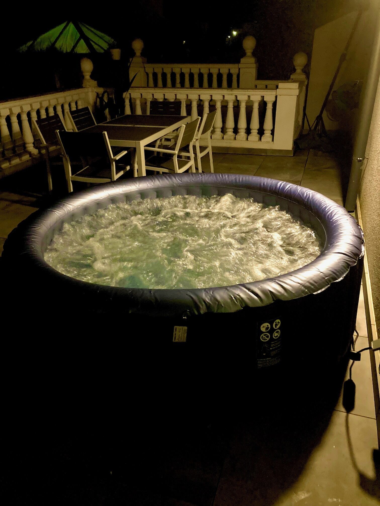 Ett bubbelbad med ett vitt räcke och ett bord med stolar i bakgrunden.