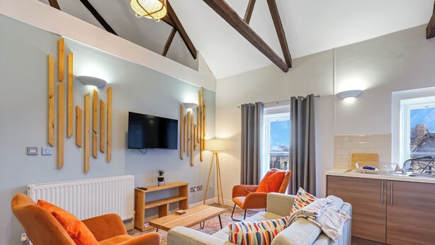 A modern living room with a sofa, chairs, a TV, and a kitchen area. - Chai- Tea Warehouse - North East Escapes (Alnwick)