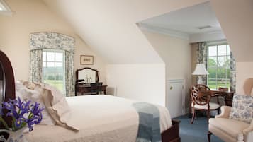 A bedroom with a large bed, a chair, a desk, and a window with curtains.