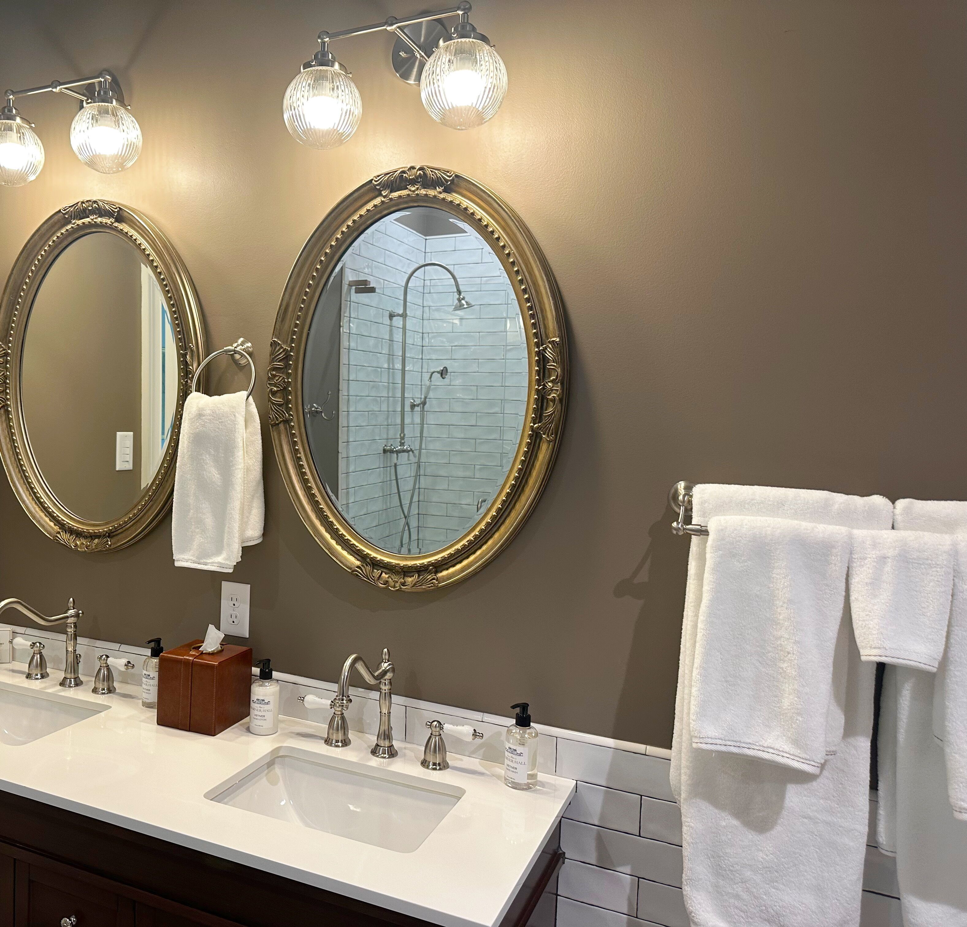 Une salle de bain dotée de deux grands miroirs, d’un lavabo avec plusieurs robinets et d’une douche avec une porte en verre.