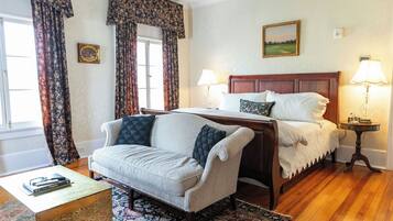 A hotel room with a wooden bed, two bedside lamps, a floral-patterned sofa, a small table with a book, and a patterned rug.