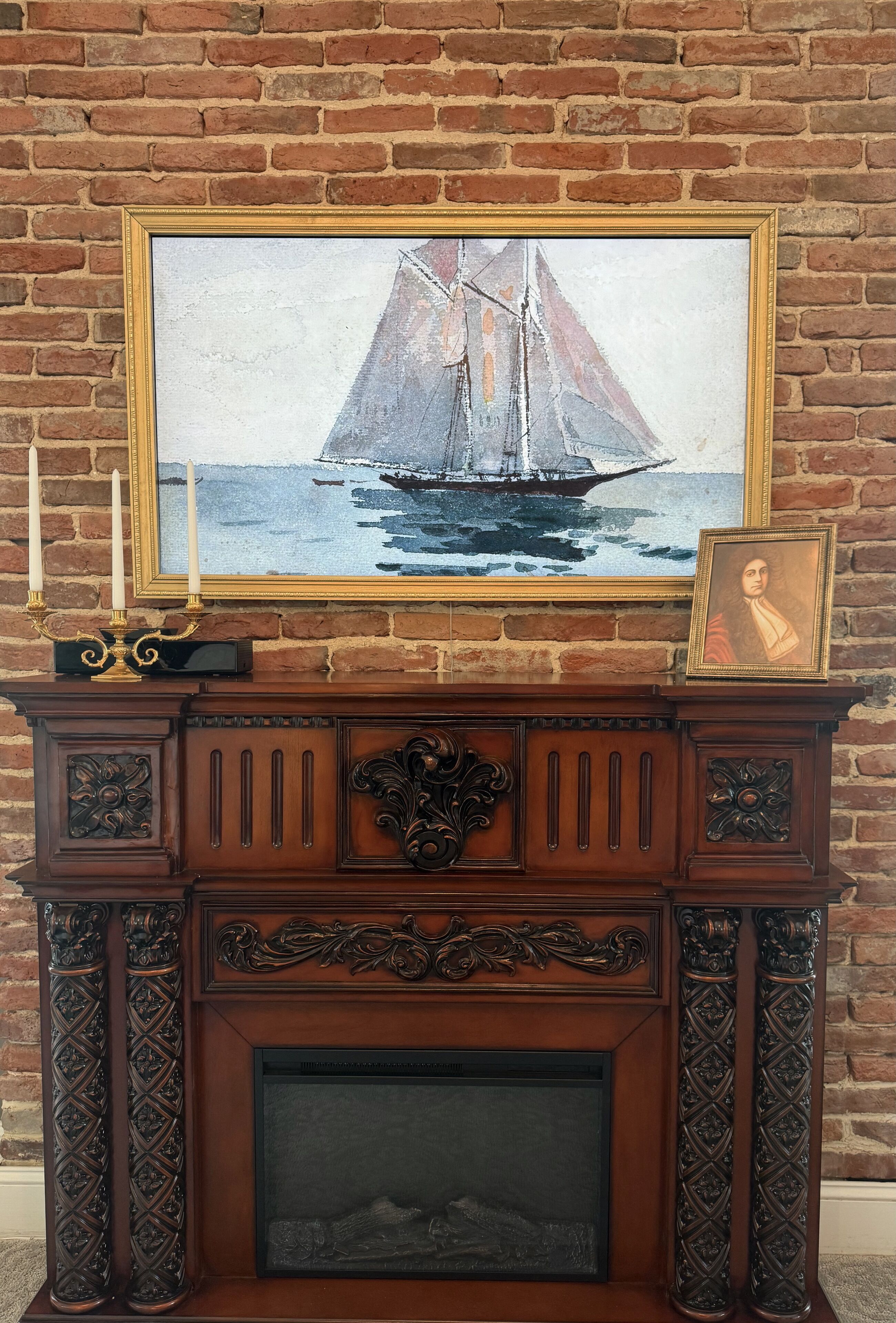 Une cheminée ornée d’un tableau encadré représentant un voilier, d’un chandelier et d’un portrait encadré placé sur le manteau de la cheminée.