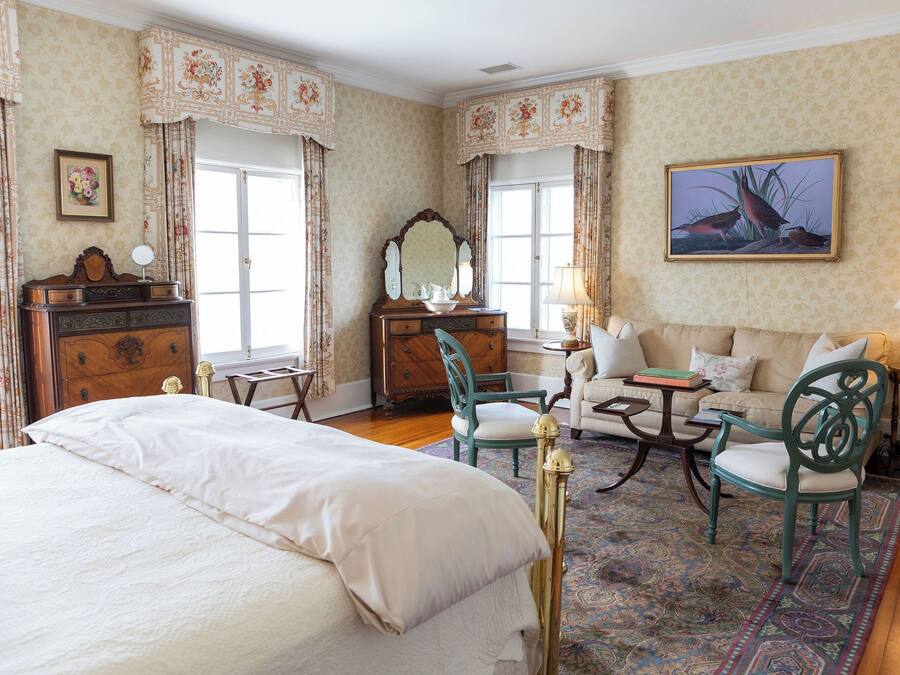 A bedroom with a large bed, a dresser, a chair, a sofa, and a painting on the wall.
