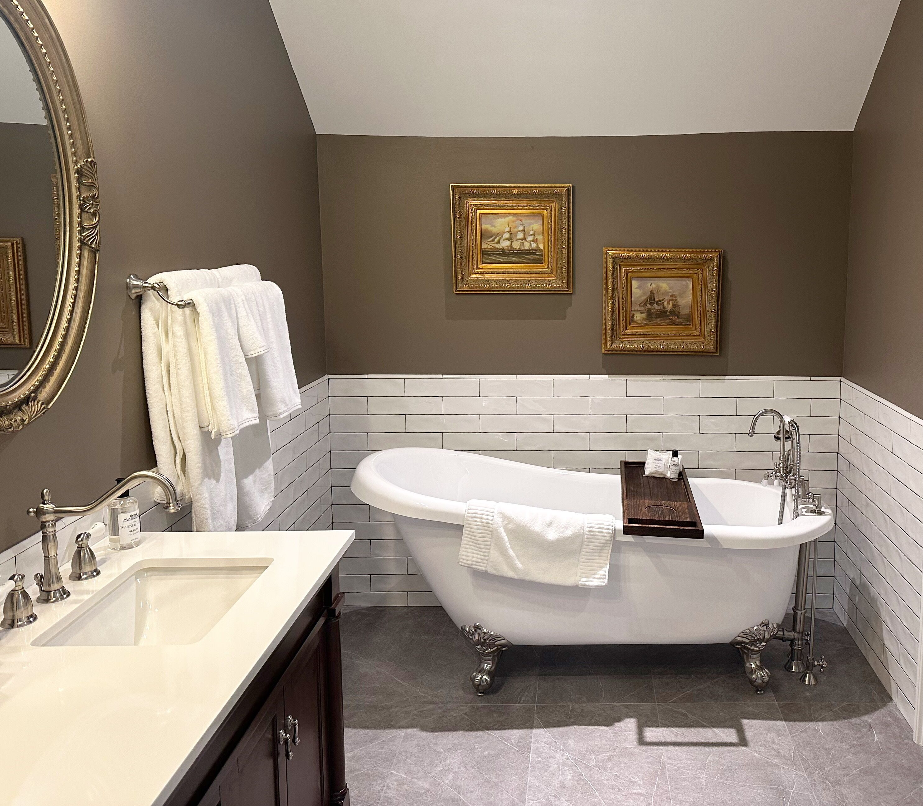 A bathroom with a freestanding bathtub, a large mirror, and two framed pictures on the wall.