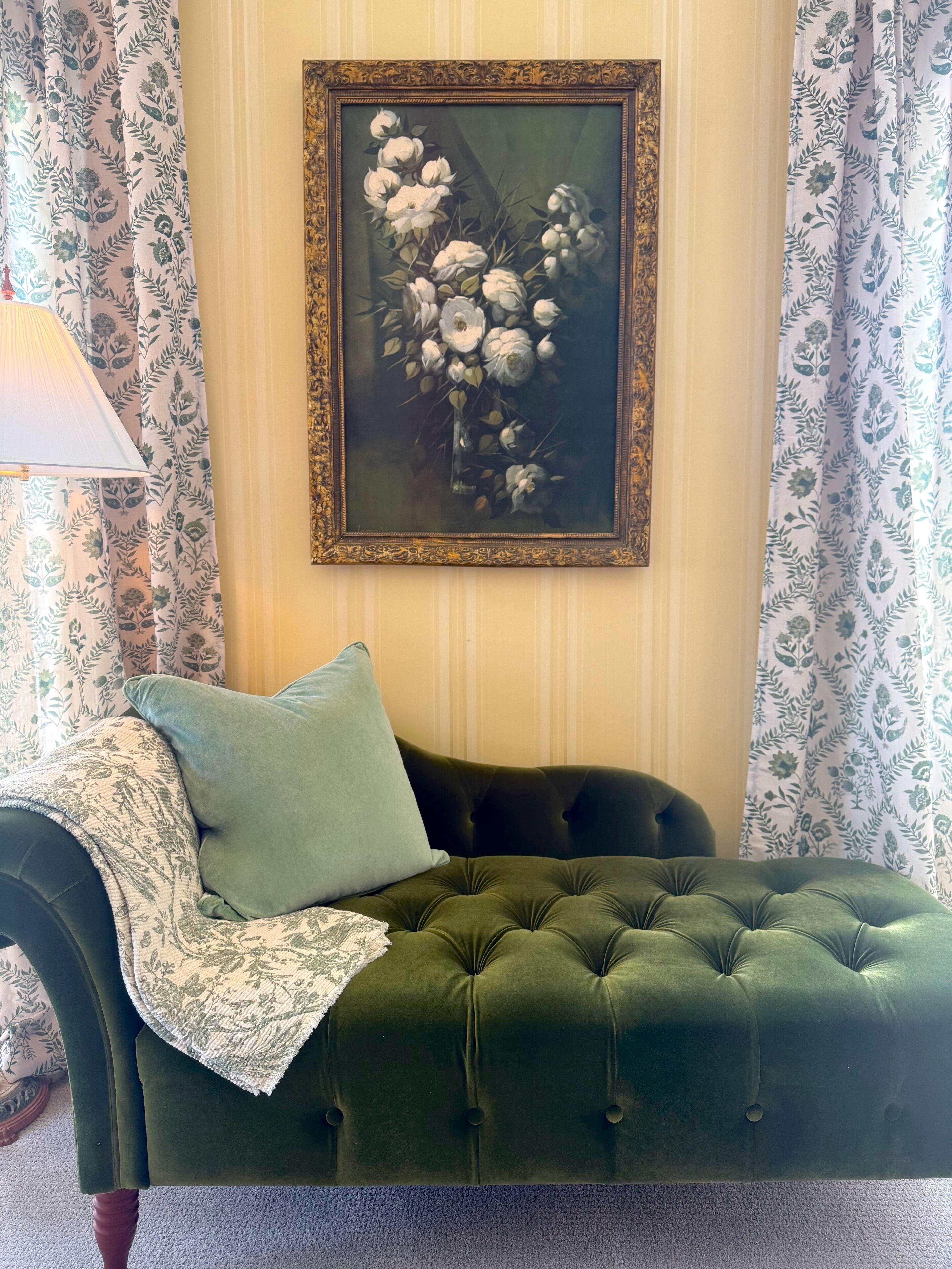Un divano verde con motivi a nido d'ape, una coperta e un cuscino, un quadro floreale incorniciato al muro e tende a fantasia.