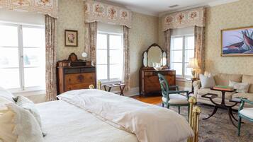 Une chambre spacieuse avec un grand lit, une commode en bois, une coiffeuse avec un miroir, un fauteuil vert et un canapé.