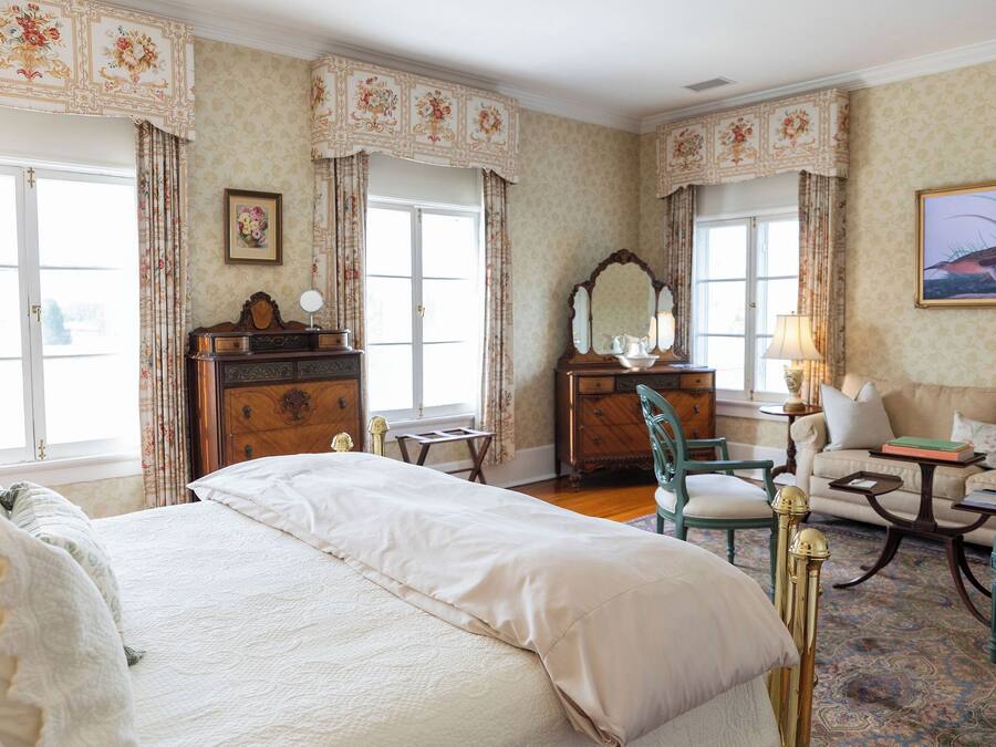 Une chambre spacieuse avec un grand lit, une commode en bois, une coiffeuse avec un miroir, un fauteuil vert et un canapé.