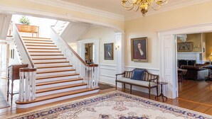 Un magnifique escalier avec des rampes blanches et des marches en bois, menant à un palier agrémenté d’un tapis à motifs et d’un banc.