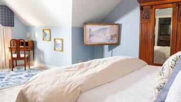 A bedroom with a bed, a wooden wardrobe, a desk with a chair, and framed artwork on the wall.