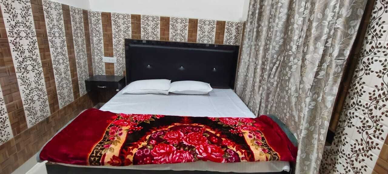 A bed with a floral-patterned bedspread, a black headboard, and a nightstand with a lamp.