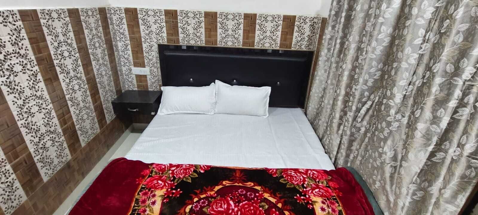 Een net opgemaakt bed met witte lakens en een bedsprei met bloemenprint, een donker hoofdbord en een nachtkastje met een klein lade.