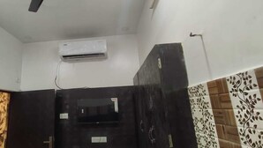 A room with a black door, an air conditioning unit mounted on the wall, and patterned tiles on the walls. - Shree Kashi Vishwanath Home Stay (Varanasi)
