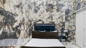 A bedroom with a bed, marble walls, and a nightstand with a lamp. - Shree Kashi Vishwanath Home Stay (Varanasi)