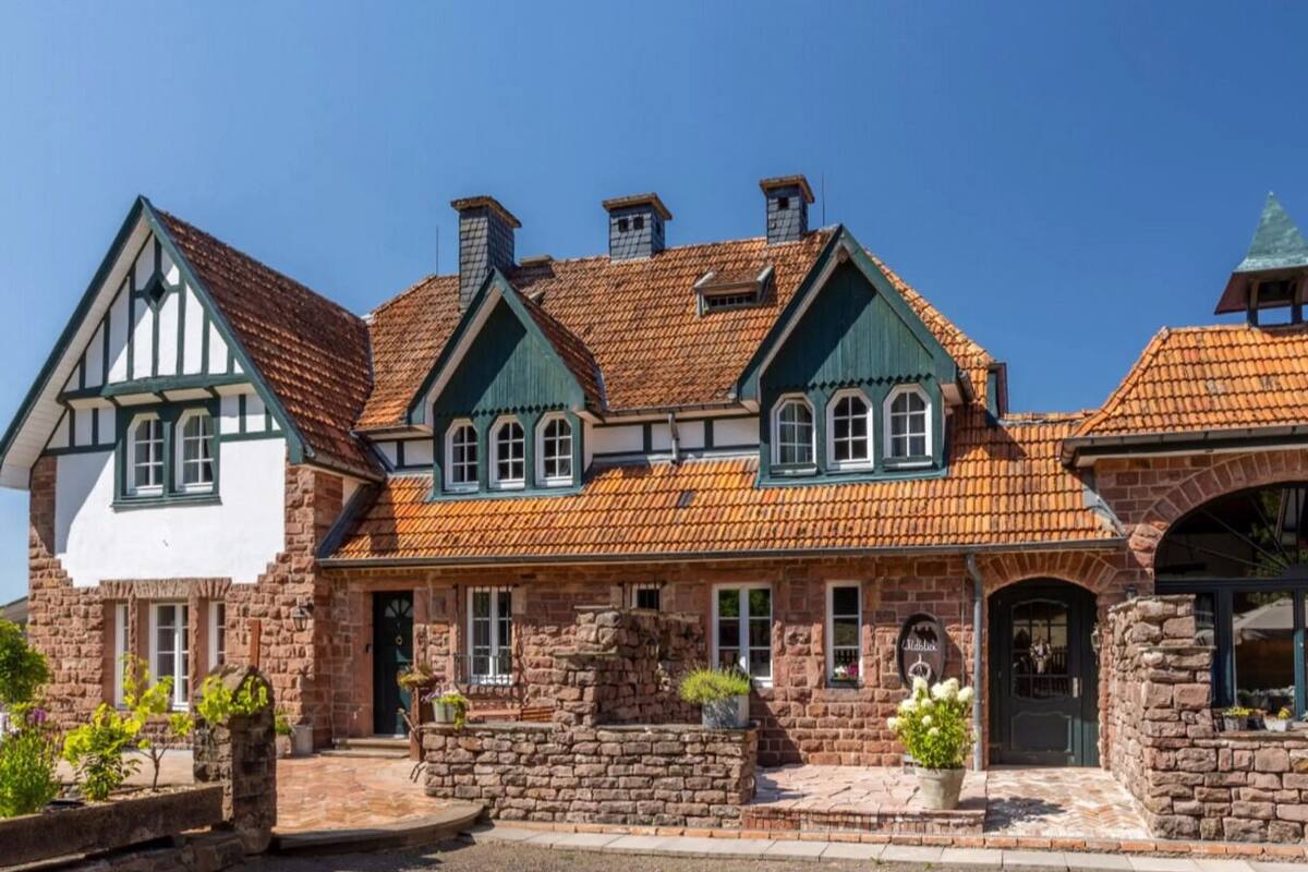 Ein traditionelles Steinhaus mit steilem Dach, mehreren Schornsteinen und einer Kombination aus weißem und grünem Fachwerk.