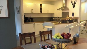 Egy modern konyha fehér szekrényekkel, központi konyhaszigettel, valamint egy étkezővel, melyben egy faasztal és székek találhatók.